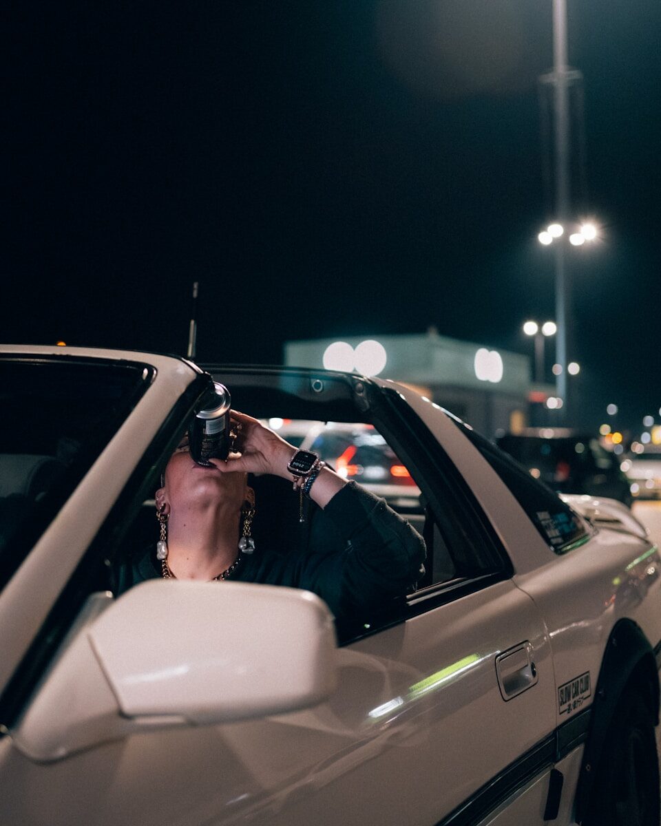 Person drinks from can inside car at night