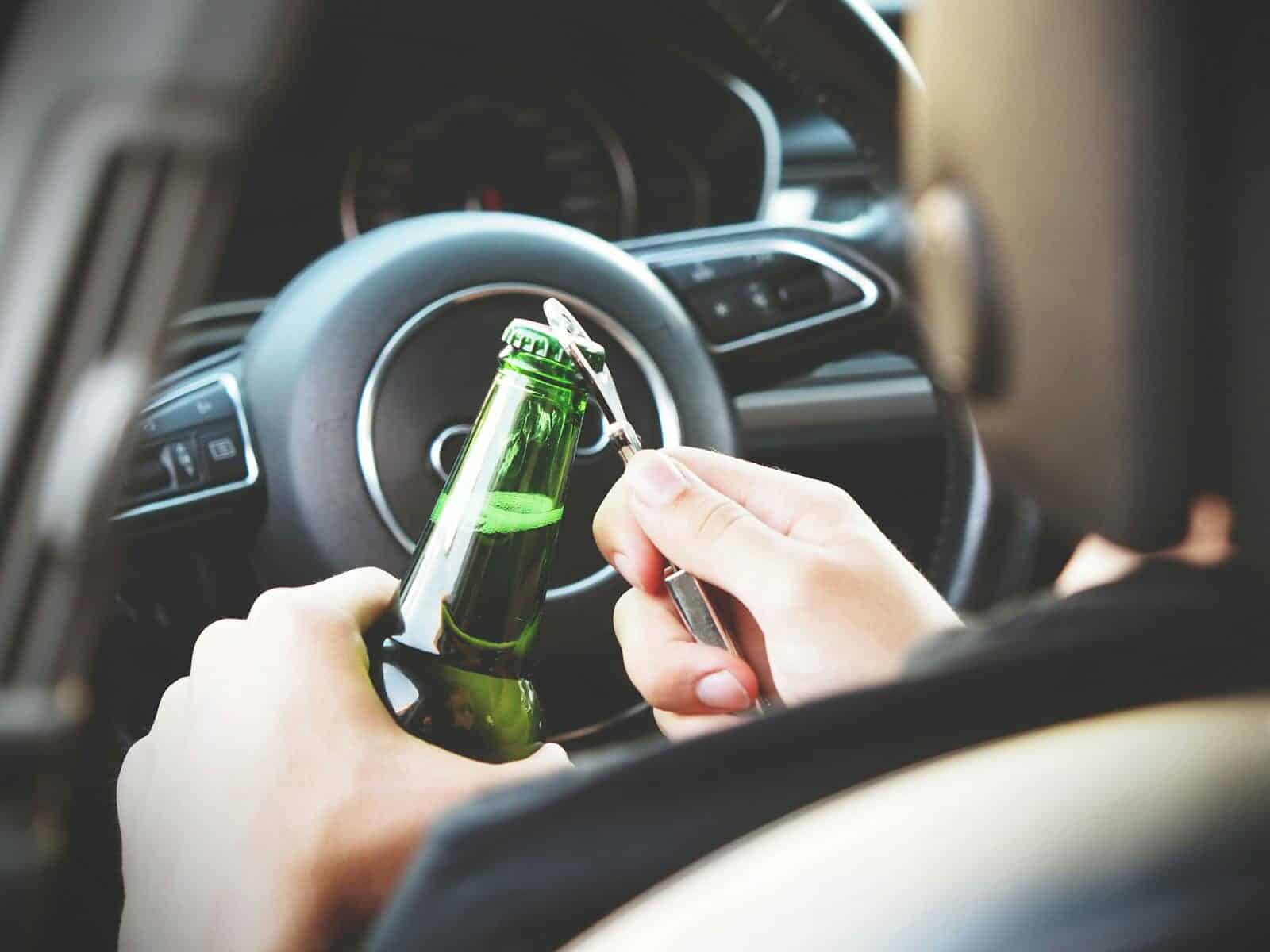 Hands opening a beer bottle inside a car, highlighting the importance of safe driving and awareness of road dangers.
