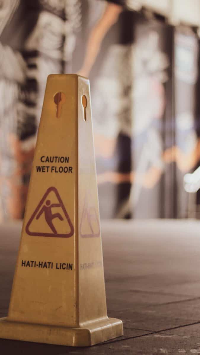 Close-up of a yellow wet floor sign with caution text in an indoor setting.