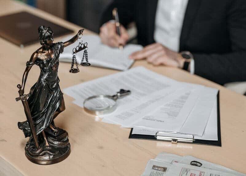 A lawyer concentrates on paperwork in an office; legal statue visible on desk.