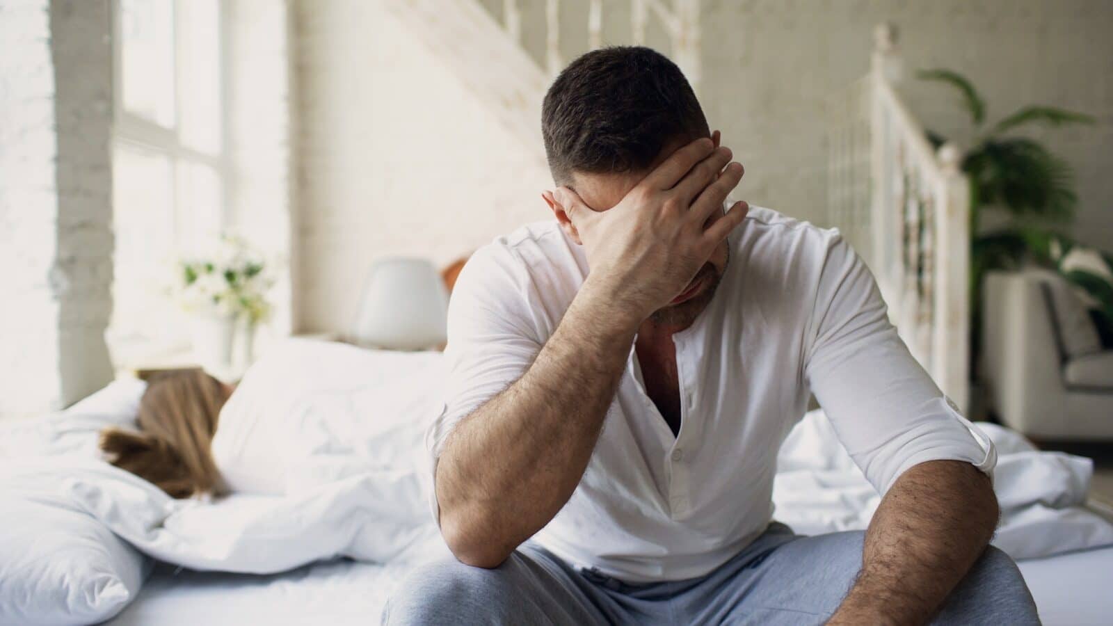 Man sitting on bed with hand over face